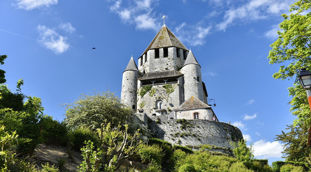 Large stone tower rising high into the blue sky with stone walls and greenery surrounding it